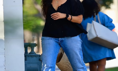 off her style in a lowcut black blouse and straight legged jeans. She paired the look with black mesh sandals